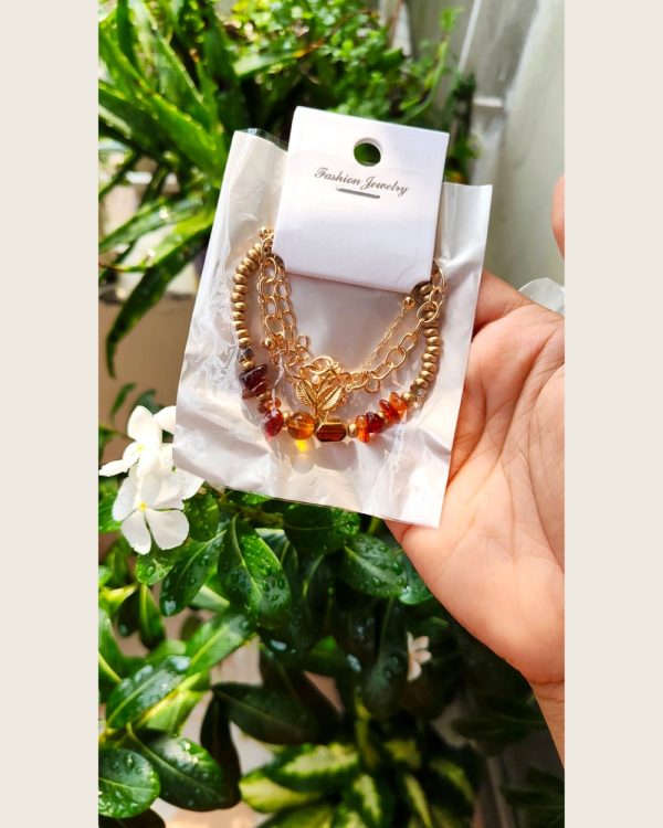 Layered gold-tone bracelet with warm amber glass beads and a leaf charm — Sira Elegance